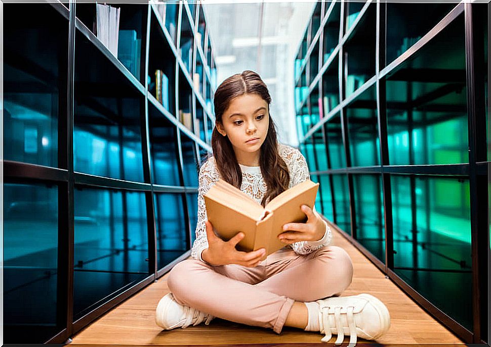 Girl reading a story with various endings sitting on the floor of a library.