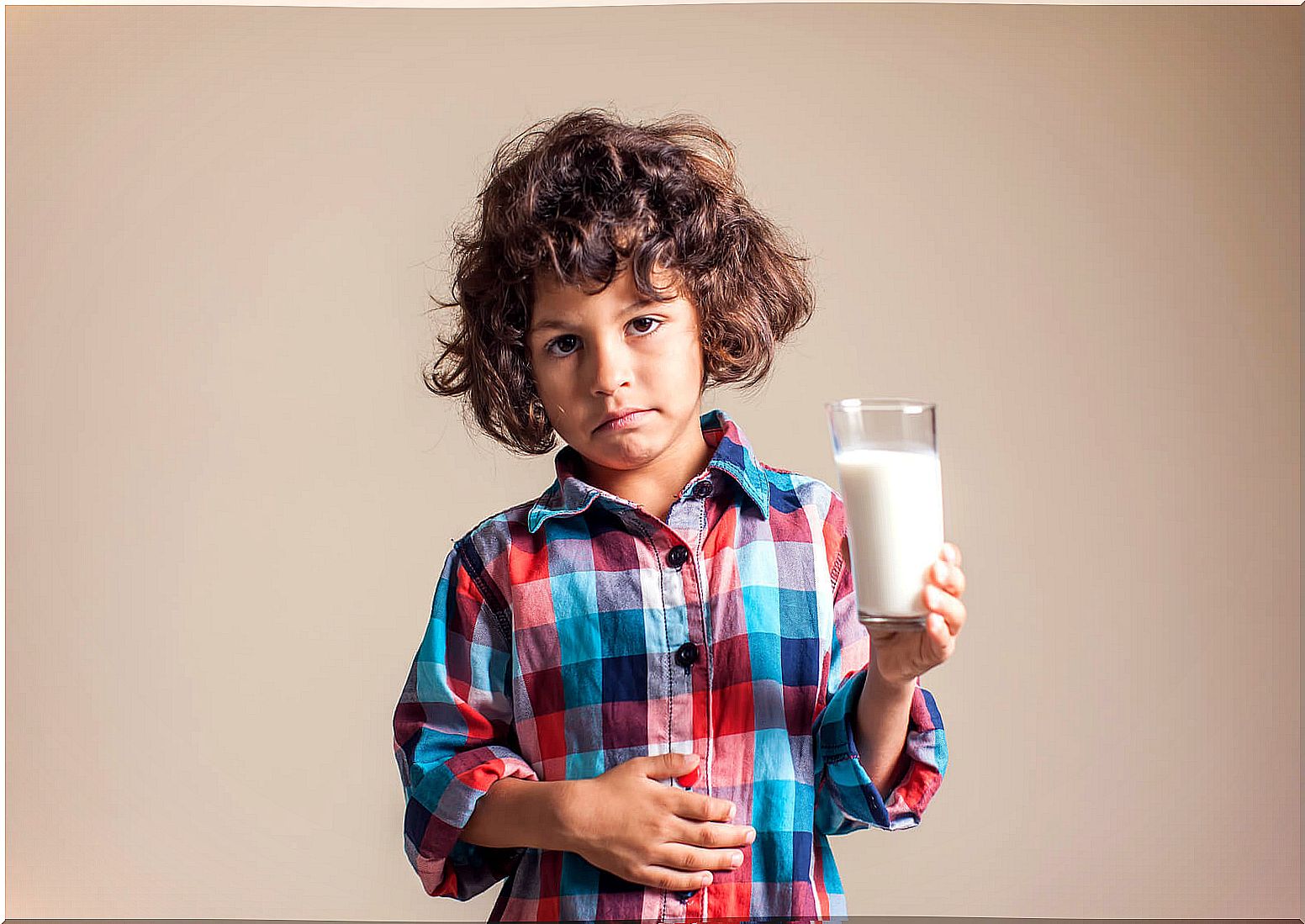 Child with a tummy ache and a glass of milk in hand due to transient lactose intolerance.