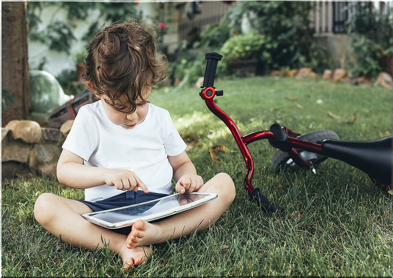 Boy playing with a tablet next to his bicycle.