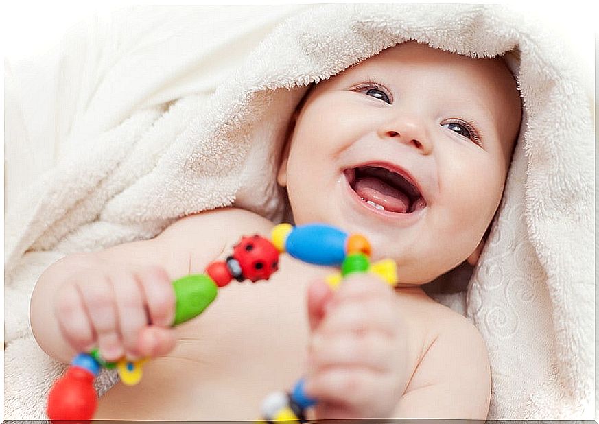 Smiling baby wrapped in a towel after a bath holds a rattle. 