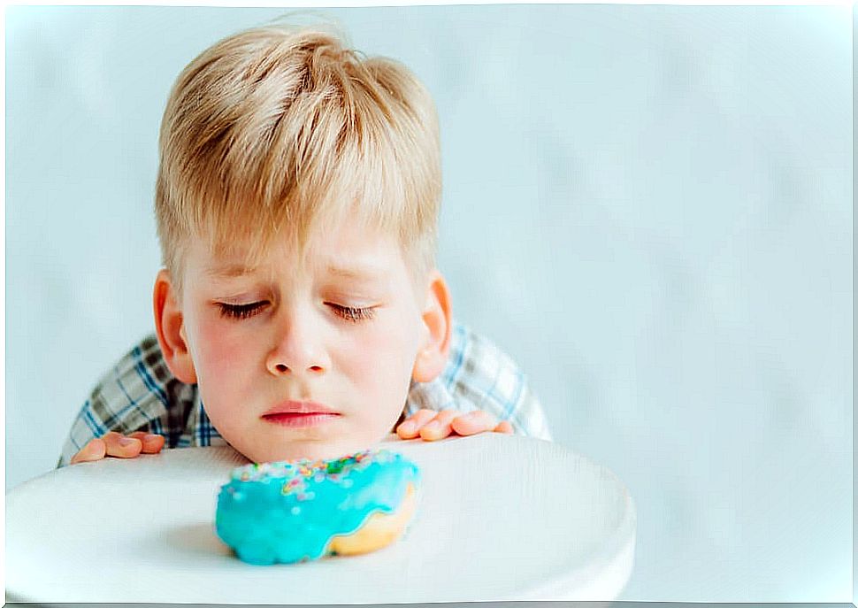 Child looking sadly at a donut because he cannot eat it due to his gluten intolerance.